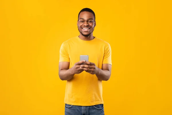 Gelukkig Afro-Amerikaanse man met behulp van telefoon staande over gele achtergrond — Stockfoto