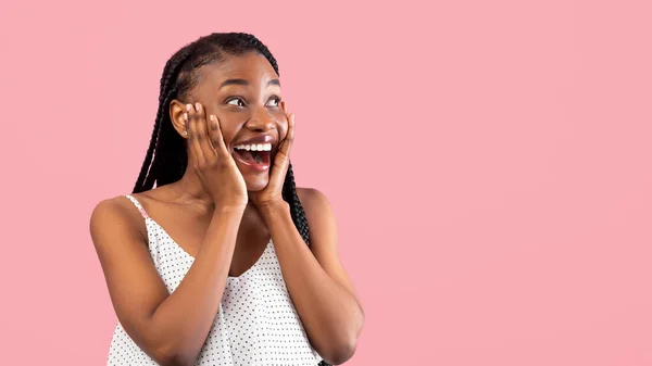 Zwarte vrouw in de zomer jurk aanraken van haar gezicht, kijken opzij naar lege ruimte in opwinding op roze studio achtergrond — Stockfoto