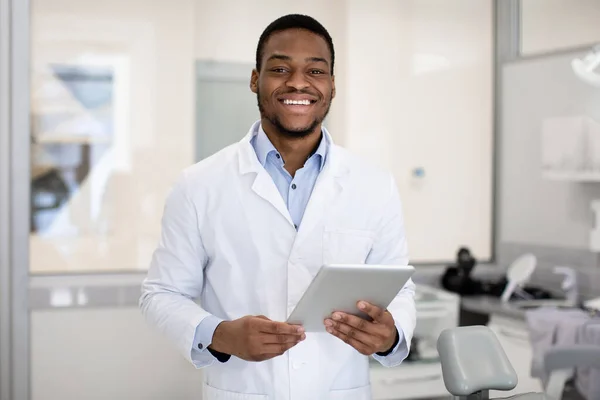 Retrato de sorrir bonito dentista preto médico com tablet digital nas mãos — Fotografia de Stock