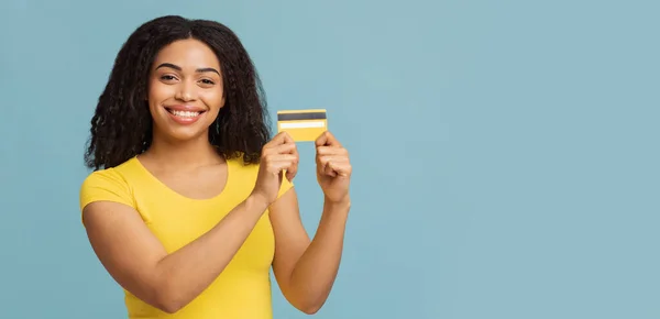 Простая концепция оплаты. Счастливая африканская американка держит кредитную карту, глядя и улыбаясь в камеру, синий фон — стоковое фото