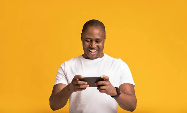 Feliz chico afroamericano atractivo muscular de mediana edad feliz en camiseta blanca jugando en el teléfono inteligente —  Fotos de Stock