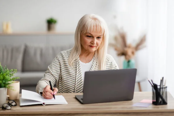 Mature woman writing and using pc laptop at home — Stock Photo, Image