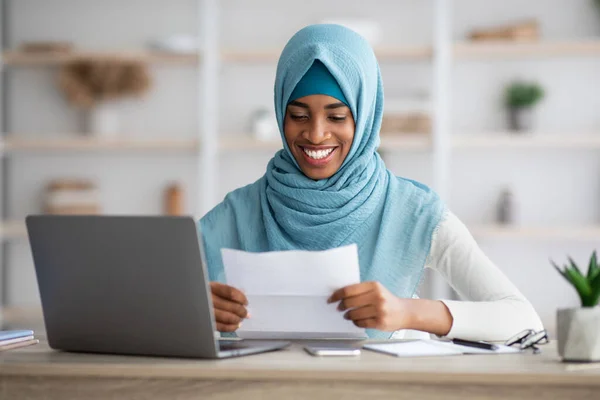 Feliz preto muçulmano mulher no hijab sentado no mesa e leitura carta — Fotografia de Stock