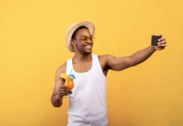 Vakáción vagyok. Mosolygós fekete srác nyáron viselni selfie trópusi gyümölcs koktél sárga stúdió háttér — Stock Fotó