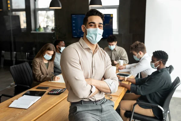 Jovem árabe empresário em máscara sentado na mesa e posando — Fotografia de Stock