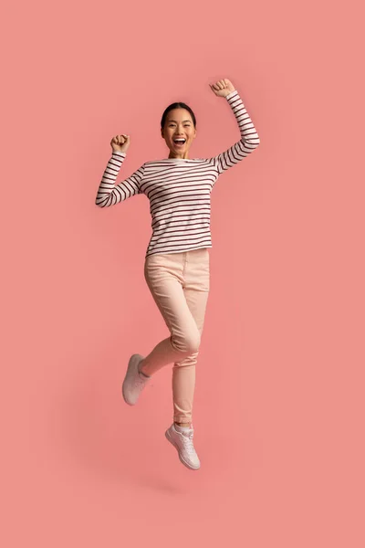Eufórico jovem ásia mulher pulando com levantado mãos sobre rosa fundo — Fotografia de Stock