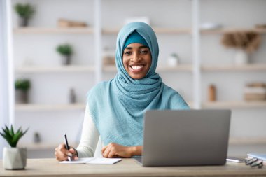 Müslüman Kadınlar İçin İş. Siyah İslami Kadın Bilgisayarla Masada Oturuyor