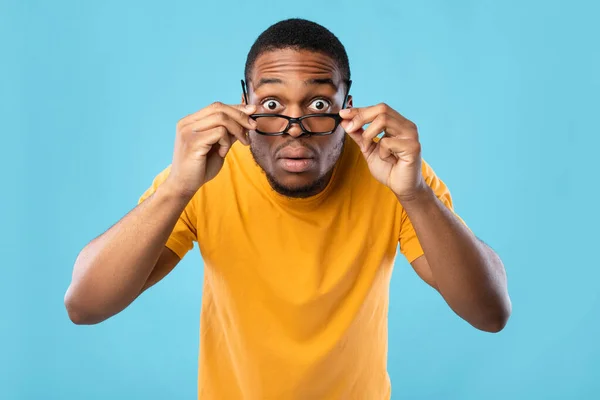Choqué homme africain regardant la caméra à travers des lunettes de vue, fond bleu — Photo