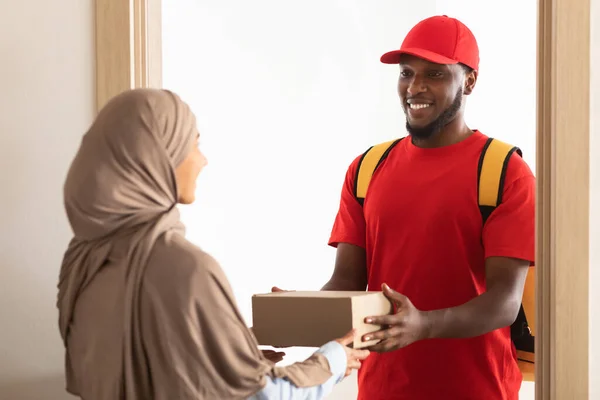 Schwarzer Liefermann hält Schachtel in der Hand und gibt sie muslimischen Kunden — Stockfoto