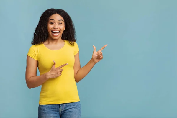 Sonderangebotskonzept. Fröhliche afrikanisch-amerikanische Dame zeigt mit dem Finger auf leeren Raum auf blauem Studiohintergrund — Stockfoto