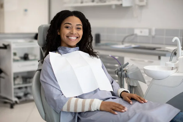 Οδοντιατρικές υπηρεσίες. Χαρούμενη χαμογελαστή μαύρη γυναίκα κάθεται στην καρέκλα στην στοματολογική κλινική — Φωτογραφία Αρχείου