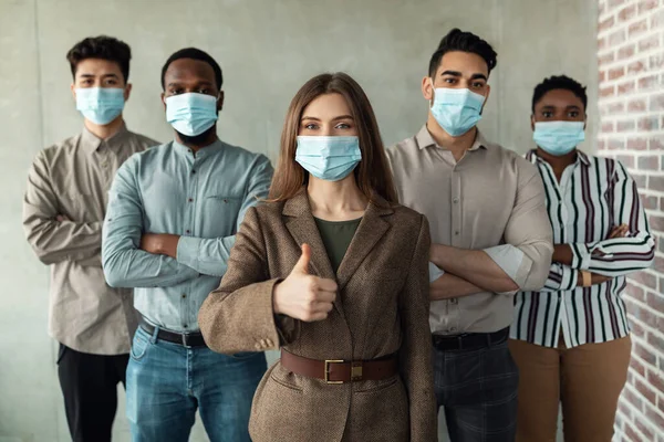 Multicultural businesspeople in masks standing in office with folded arms