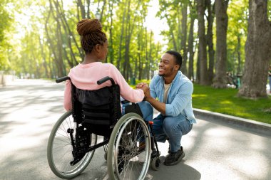 Hassas siyah adam engelli kız arkadaşının elini tutuyor. Şehir parkında sevgisini ve sevgisini ifade ediyor.