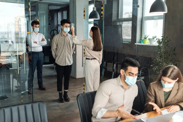 Worker with contactless thermometer measuring temperature of multiracial employees — Stock Photo, Image