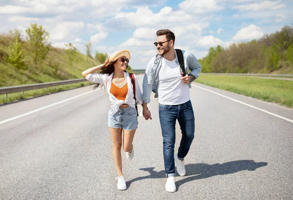 Full längd av positiva unga par promenader längs motorvägen, hålla händer, ha kul tillsammans utomhus — Stockfoto