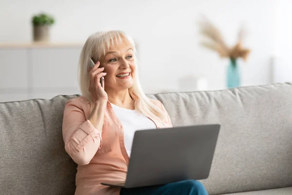 Glimlach volwassen vrouw werken en praten op mobiele telefoon thuis — Stockfoto