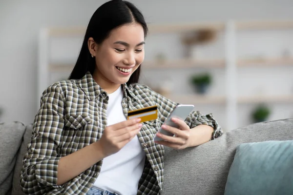 Cheerful chinese woman holding smartphone and credit card — Stock Photo, Image