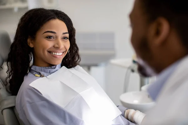 Conceito de Estomatologia. Sorrindo mulher negra sentada na cadeira na clínica dentária — Fotografia de Stock