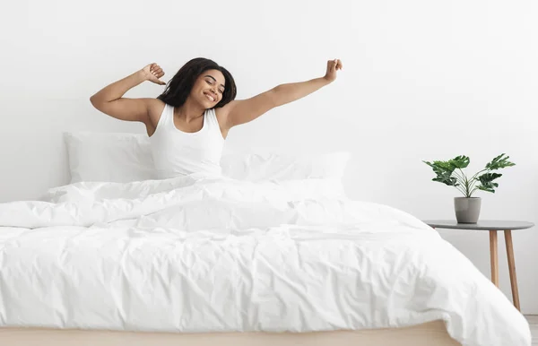 Buenos días, nuevo día. Emocionada dama afroamericana sentada en la cama, estirando los brazos después del sueño, espacio vacío —  Fotos de Stock