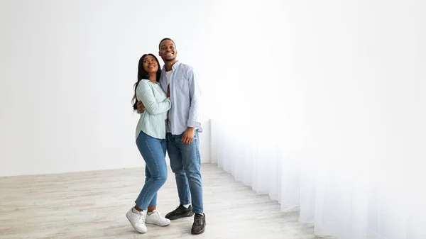 Concetto immobiliare. Felice coppia afroamericana in piedi in camera bianca vuota del loro nuovo appartamento, spazio vuoto — Foto Stock