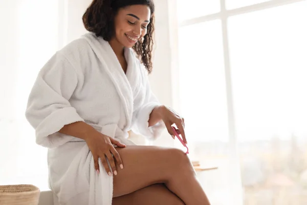 Красивая африканская молодая женщина делает депиляцию бритья ног в ванной комнате — стоковое фото