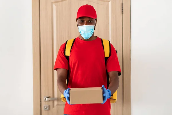 Homem de entrega preto em máscara médica segurando caixa — Fotografia de Stock