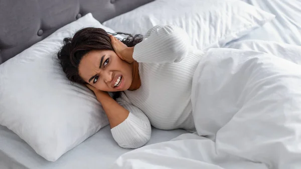 Mujer negra enojada cubriendo orejas acostadas en la cama —  Fotos de Stock