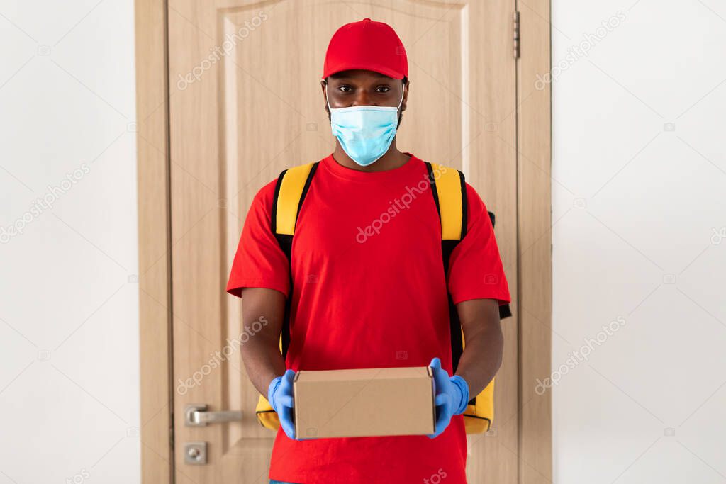 Black delivery man in medical mask holding box
