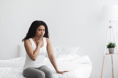 Farenjit. Hasta zenci kadın boğazına dokunuyor, kötü hissediyor ve öksürüyor, evde yatakta oturuyor, boş yer var.