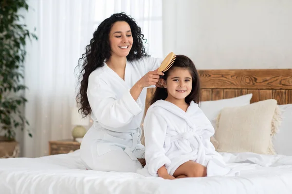 Mãe alegre escovando seu bonito filha longo cabelo encaracolado — Fotografia de Stock