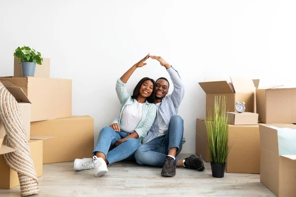 Genç aileler için ipotek. Kendi evlerine taşınan mutlu siyah çift, sembolik ev çatısı yapmak için el ele tutuşuyorlar. — Stok fotoğraf
