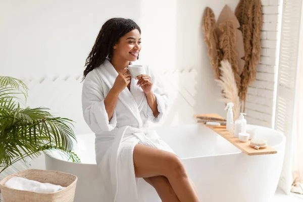 Gelukkig Afrikaans dame drinken koffie zitten op bad in de badkamer — Stockfoto
