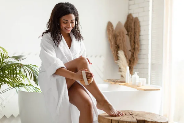 Afrikaanse dame droge borstelen benen met behulp van massage borstel in de badkamer — Stockfoto