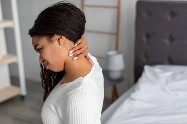 Портрет черной женщины с болью в шее, сидящей на кровати — стоковое фото