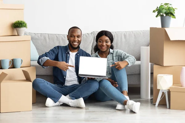 Черные супруги указывают на ноутбук с чистым экраном в своем новом доме — стоковое фото