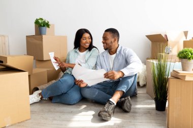 Genç bir ailenin ev tasarımını düşünmesi, daire planını tutması, eşyalarla dolu kutuların arasında oturması.,