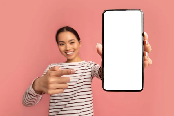 Sorrindo mulher asiática apontando no smartphone com tela branca em branco nas mãos — Fotografia de Stock