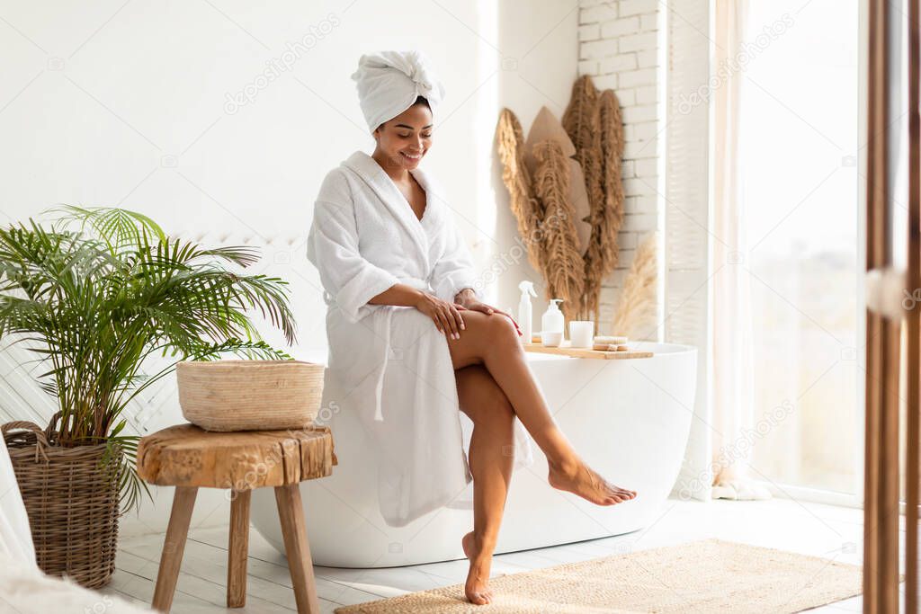 African Female Touching Smooth Legs After Depilation Sitting In Bathroom