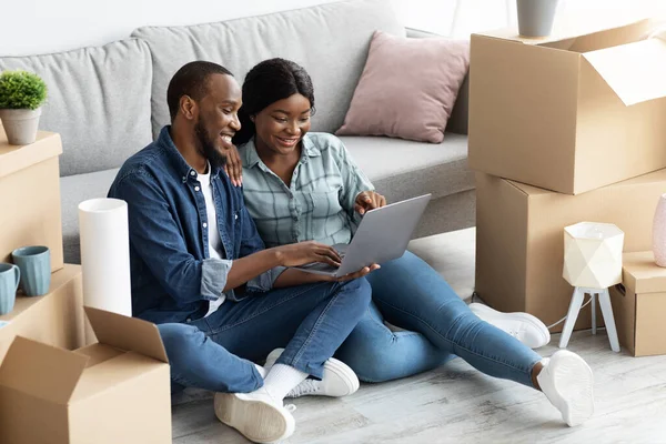 Jovens cônjuges africanos felizes usando laptop depois de se mudar para a nova casa — Fotografia de Stock