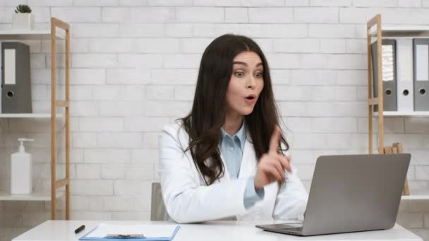 Feliz médico femenino que tiene una gran idea usando el ordenador portátil en la oficina — Vídeos de Stock