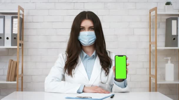 Médico feminino mostrando tela do celular vestindo máscara facial no escritório — Vídeo de Stock