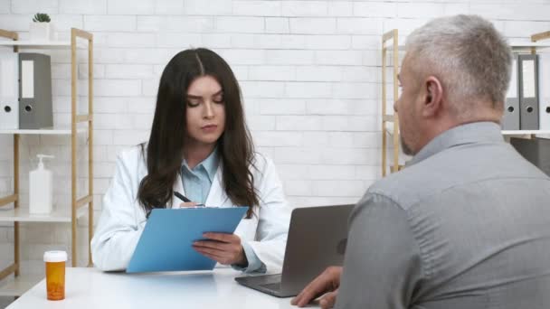 Praktikant mluví s nemocným starším pacientem psaní poznámek v kanceláři — Stock video