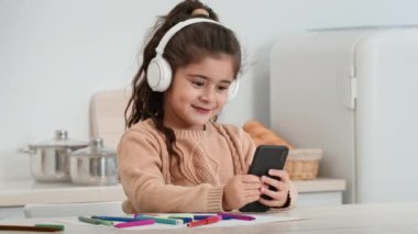 Mutlu küçük kız evde mutfaktaki akıllı telefonu kullanıyor.