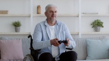Engelli adam video oyunu oynuyor. Tekerlekli sandalyede oturmuş içeride eğleniyor.