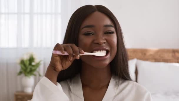 Mujer negra limpiando dientes con cepillo de dientes de pie en el dormitorio — Vídeo de stock