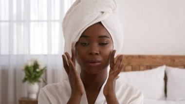 Göz kamaştırıcı siyah kadın nemlendirici krem sürüyor. Yatak odasına dokunuyor.