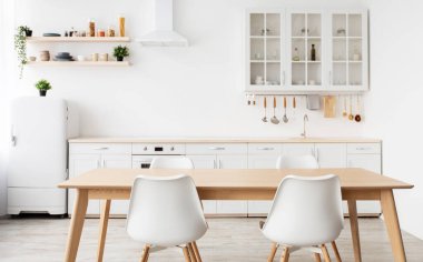 İskandinav iç tasarımı. Hafif mutfak mobilyaları ve yemek masası, raflarda farklı mutfak gereçleri ve mutfak malzemeleri.