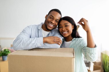 Emlak konsepti. Afro-Amerikan genç eşleri sevmek taşınan kutular ve yeni ev anahtarlarıyla poz vermek