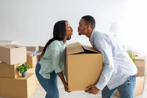Verhuisconcept. Houden van Afrikaans Amerikaans paar dragen grote kartonnen doos en proberen te kussen — Stockfoto