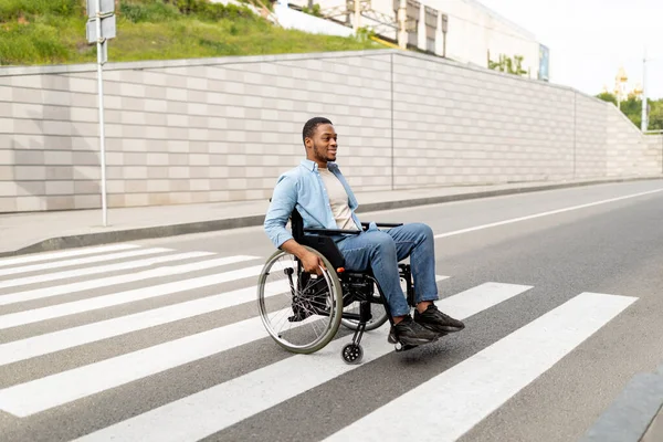Teljes hosszúságú portré fogyatékos fiatal fekete srác tolószékben átkelés a város utcáján, másolás tér — Stock Fotó